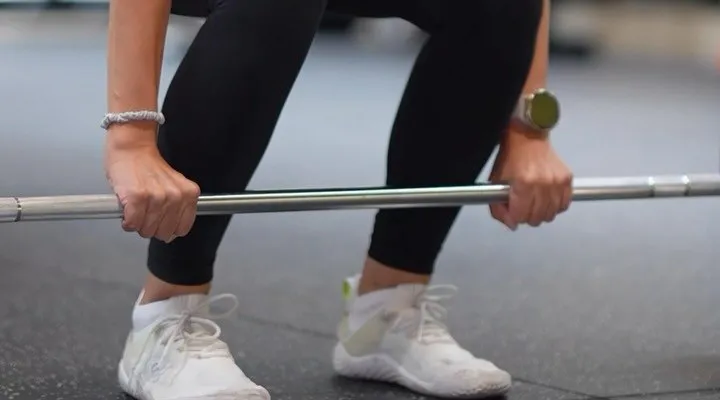 Hands gripping a barbell before a deadlift, white trainers on the rubber floor