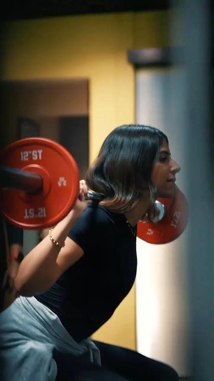 A member back-squats a barbell loaded with red plates at Enclave