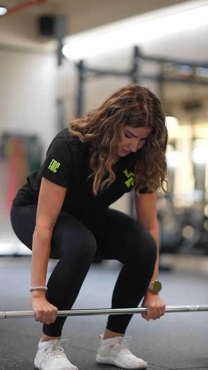 Coach Sarah sets up a deadlift in an Enclave T-shirt, squat rig behind her